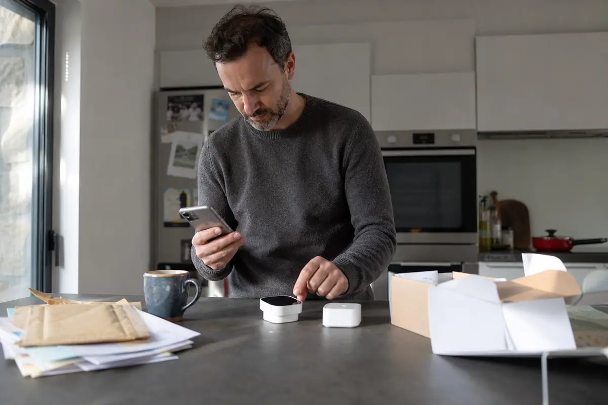 Un homme compare deux thermostats connectés sur son plan de travail en consultant une application