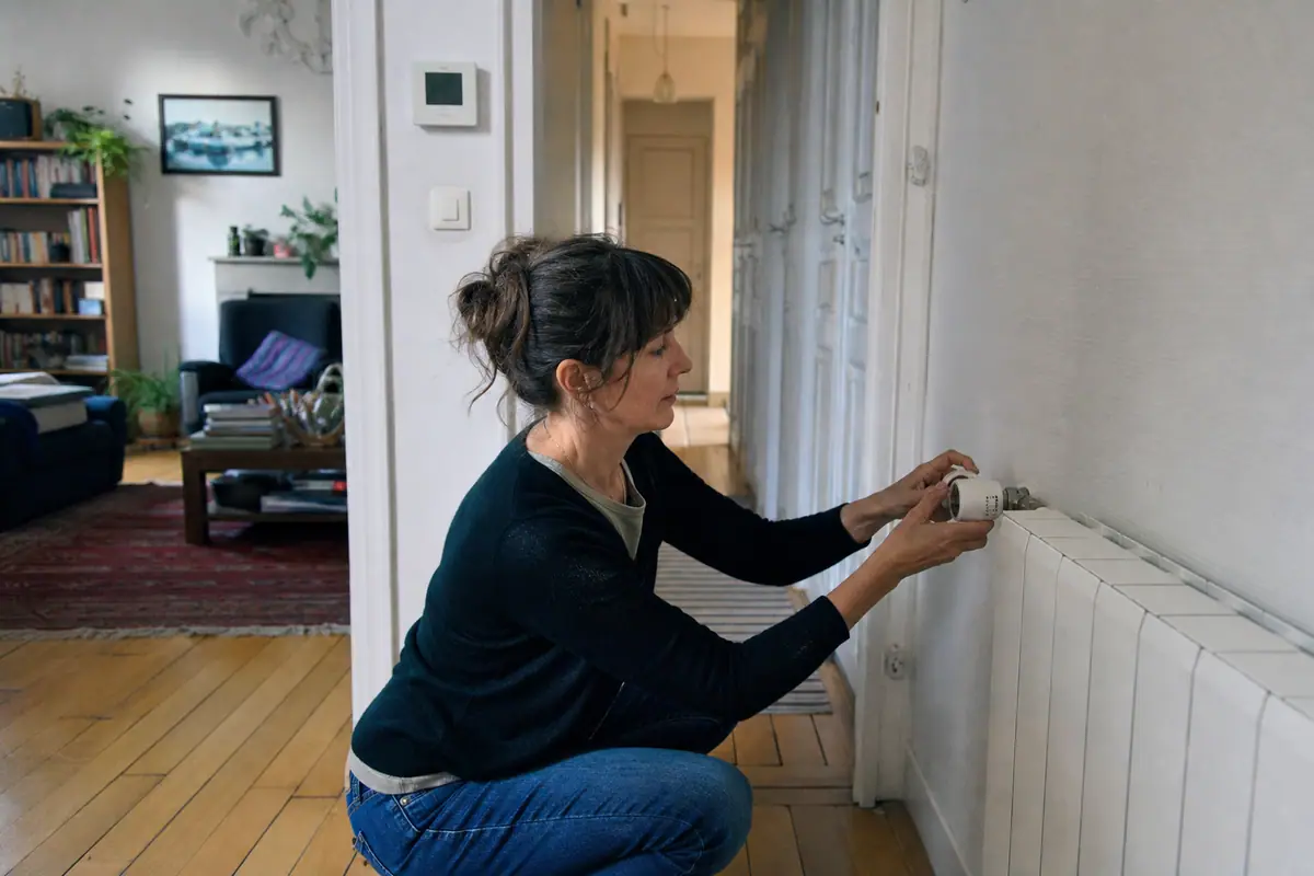 Une femme règle une tête thermostatique connectée sur un radiateur dans son salon