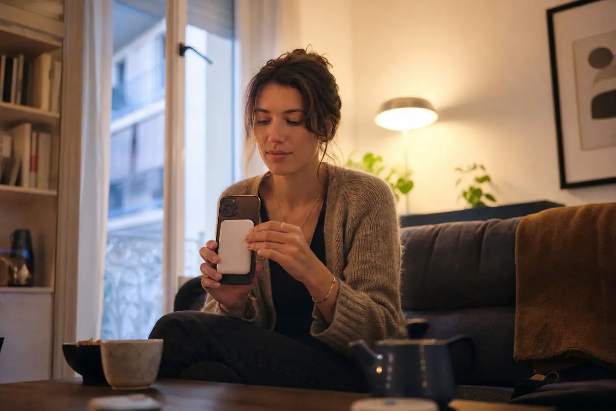 Une jeune femme fixe une batterie externe magnétique au dos de son smartphone dans son salon