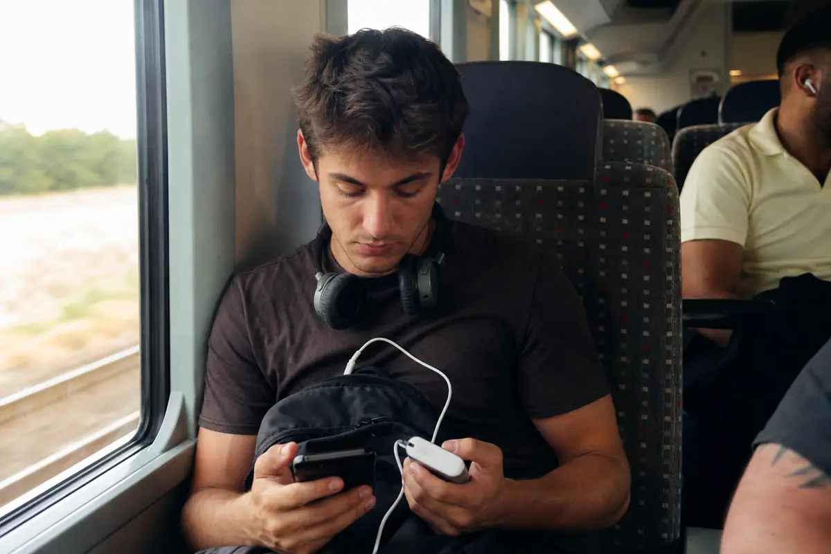 Un jeune homme recharge son smartphone avec une batterie externe pendant un trajet en train