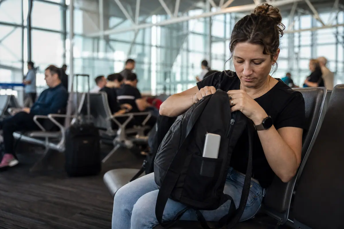 Une voyageuse vérifie sa batterie externe dans son sac à l'aéroport avant l'embarquement