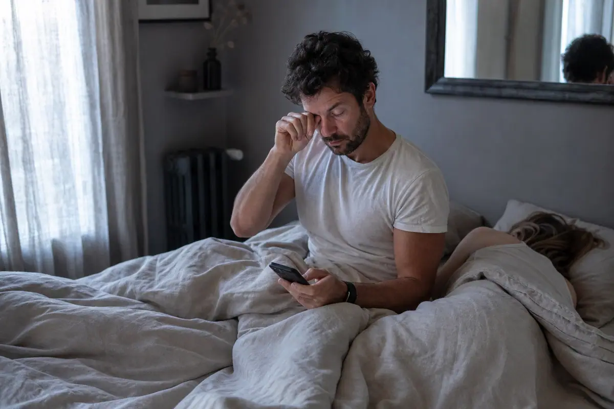 Un homme consulte au réveil l'analyse de sa nuit sur son téléphone, un bracelet connecté au poignet