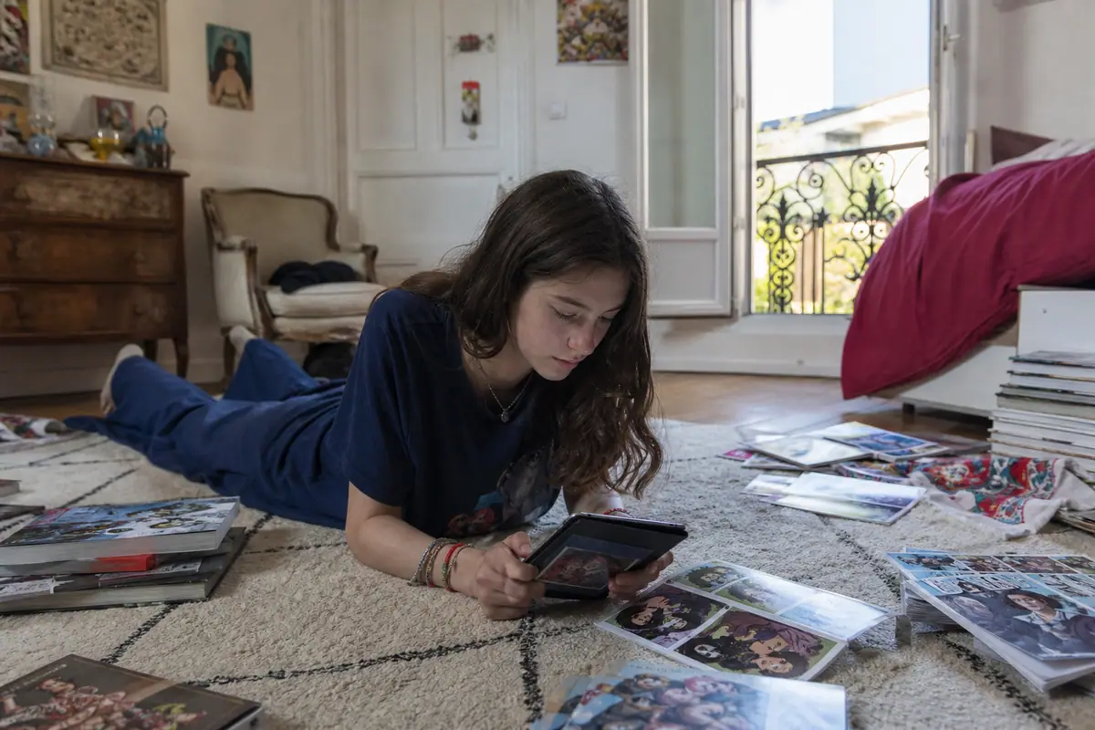 Une adolescente allongée sur un tapis lit une bande dessinée en couleur sur une liseuse