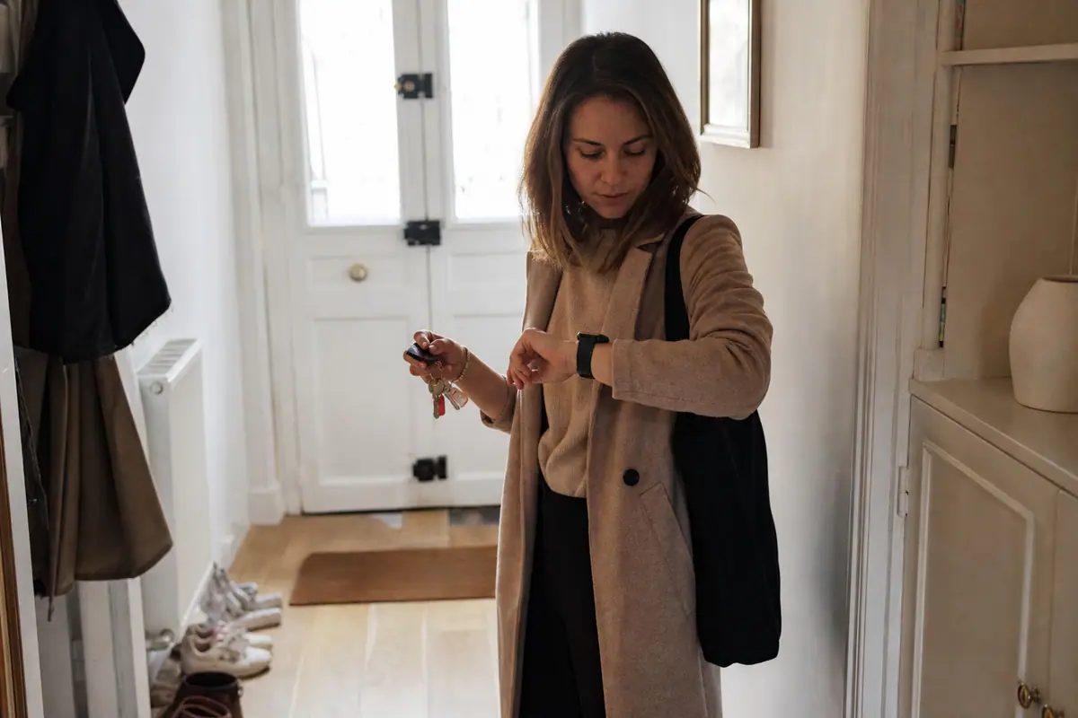 Une femme consulte une notification sur sa montre connectée dans l'entrée de son appartement avant de partir travailler