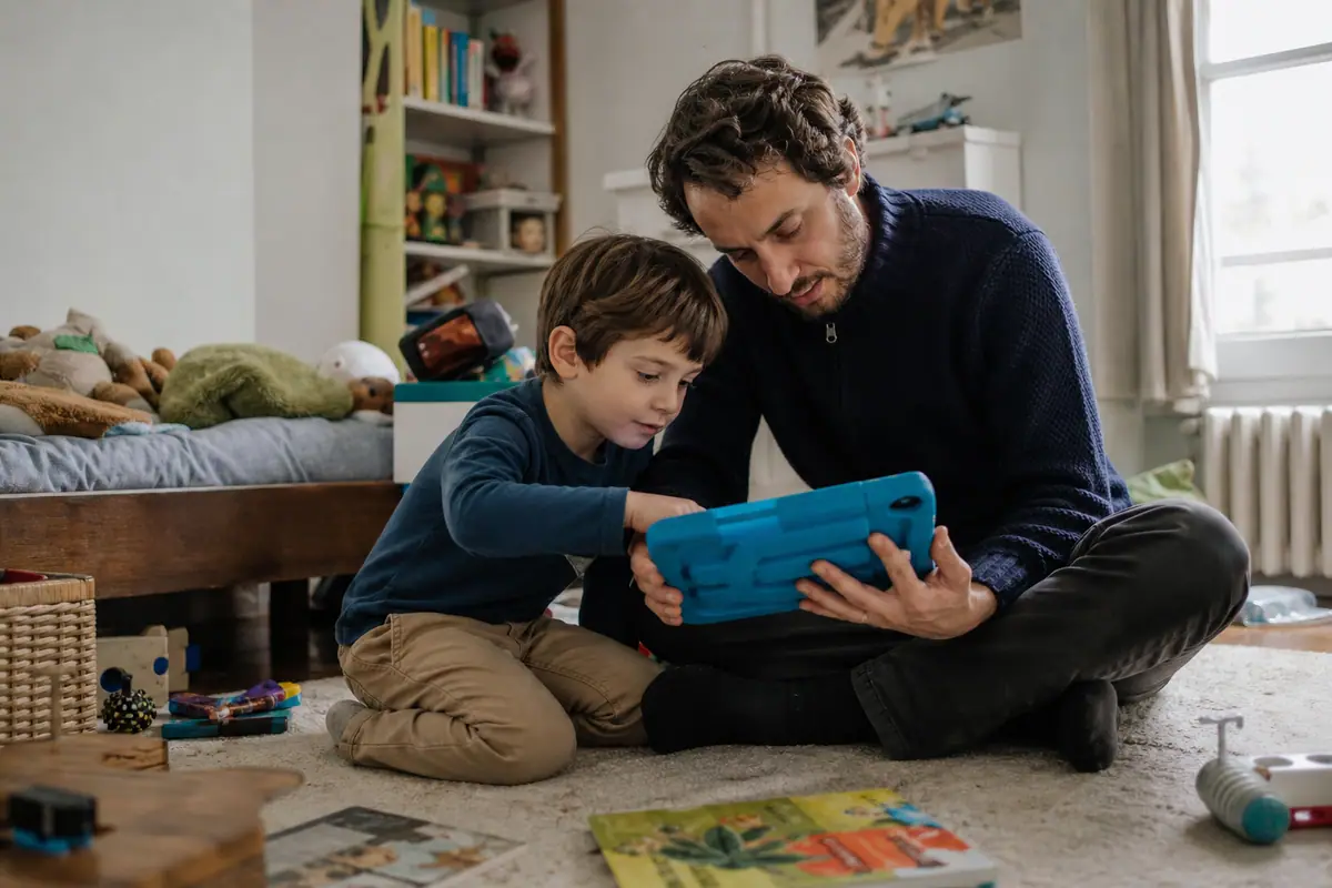 Un père configure une tablette dans une coque de protection avec son fils de sept ans dans sa chambre