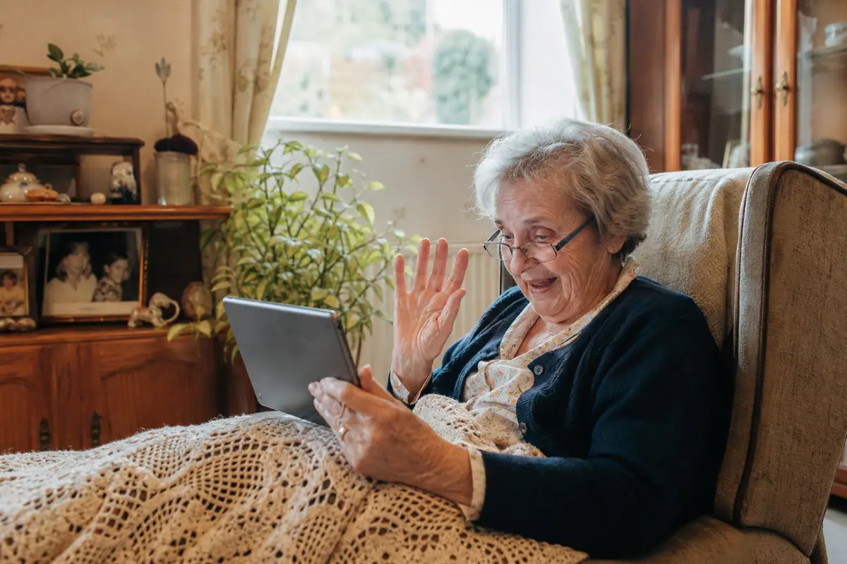 Une grand-mère sourit en appel vidéo avec ses petits-enfants sur une tablette tactile dans son salon
