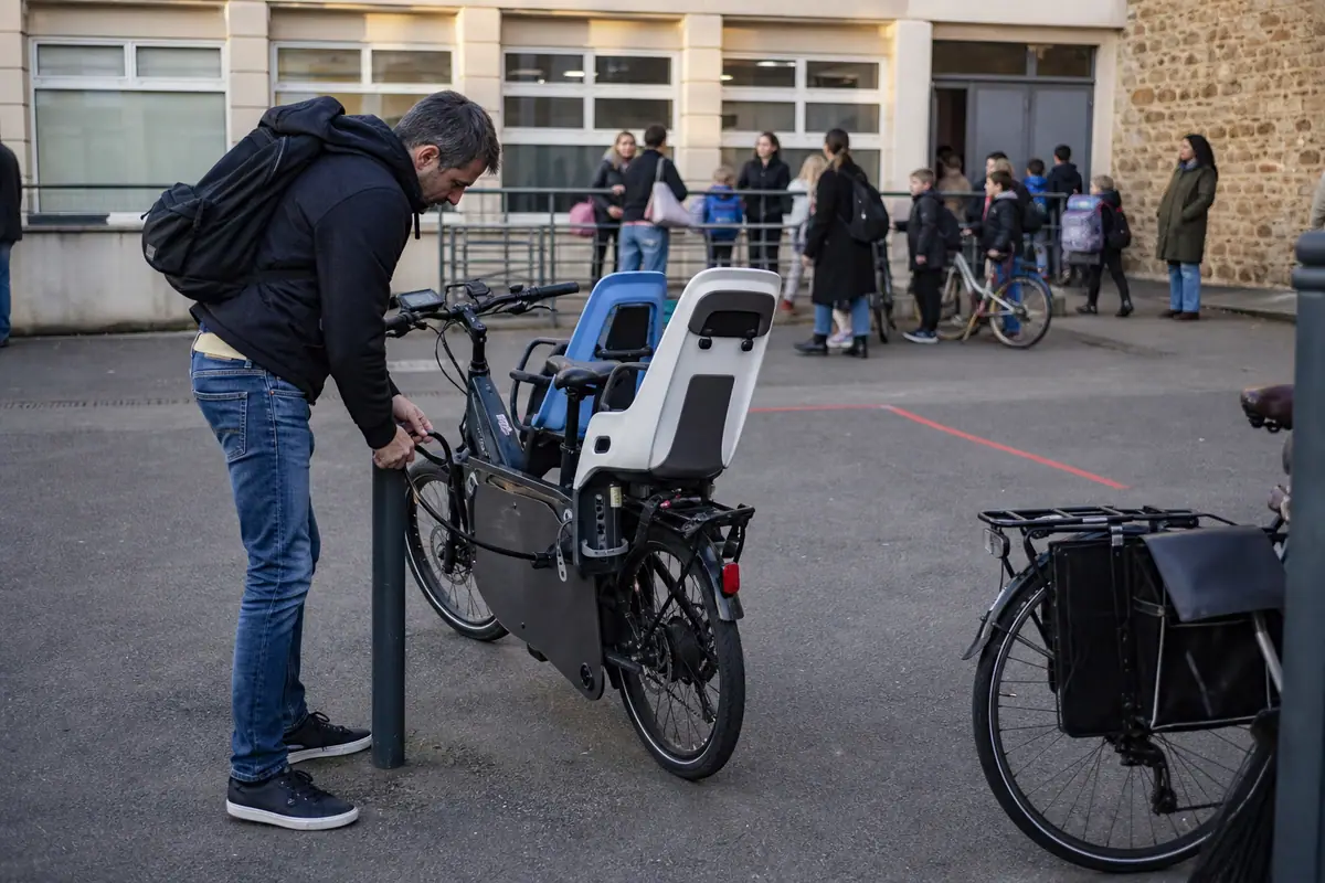 Un père attache son vélo cargo électrique avec un antivol renforcé devant une école