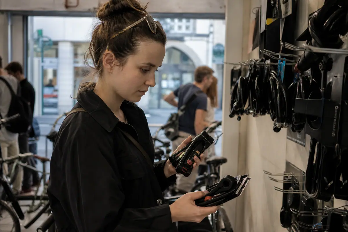 Une jeune femme compare le prix de deux antivols affichés sur un présentoir en magasin de vélos