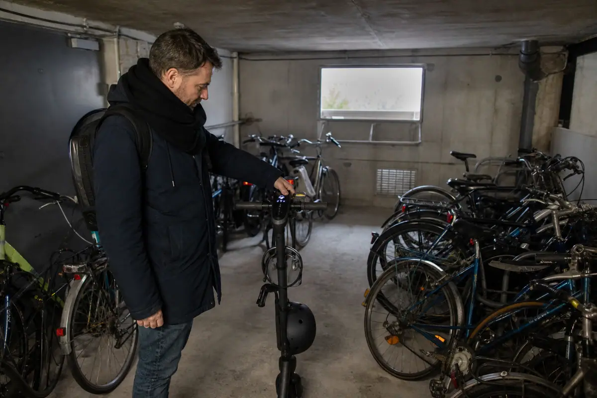 Un homme vérifie le niveau de batterie de sa trottinette électrique avant de partir travailler dans un local à vélos