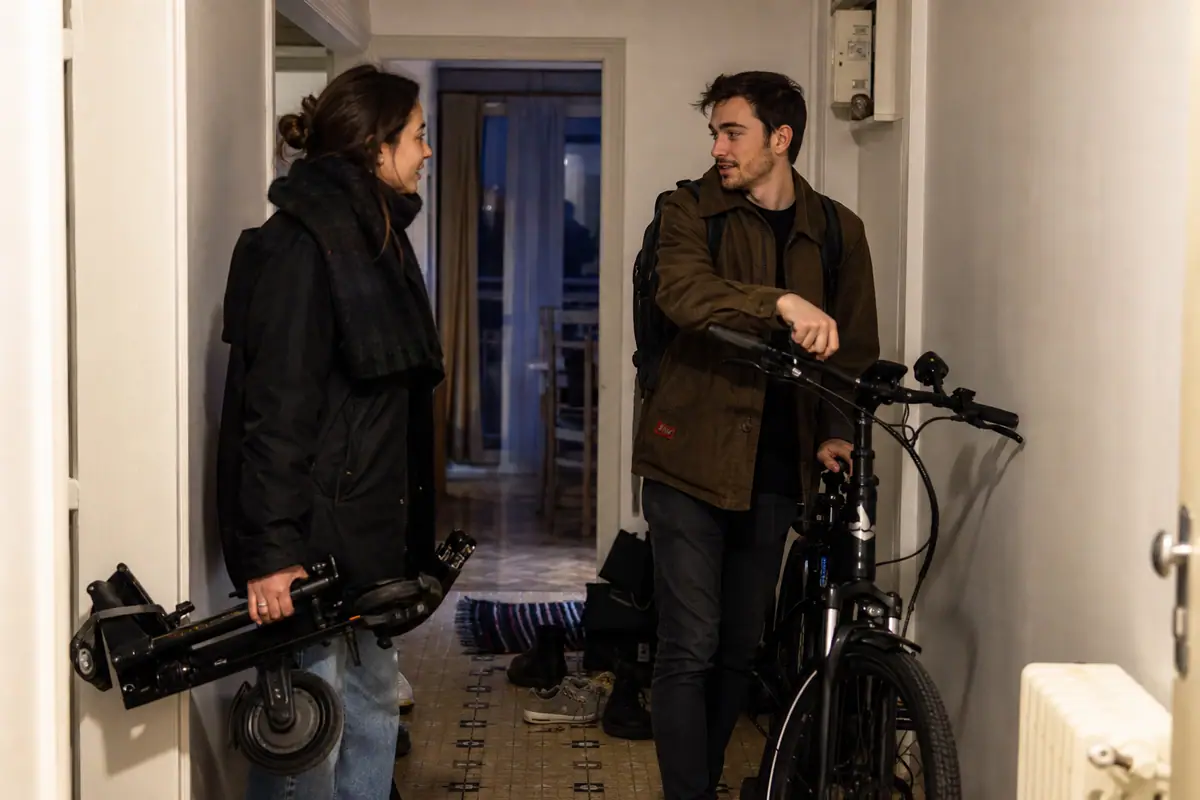 Un couple range une trottinette électrique et un vélo électrique dans l'entrée de son appartement