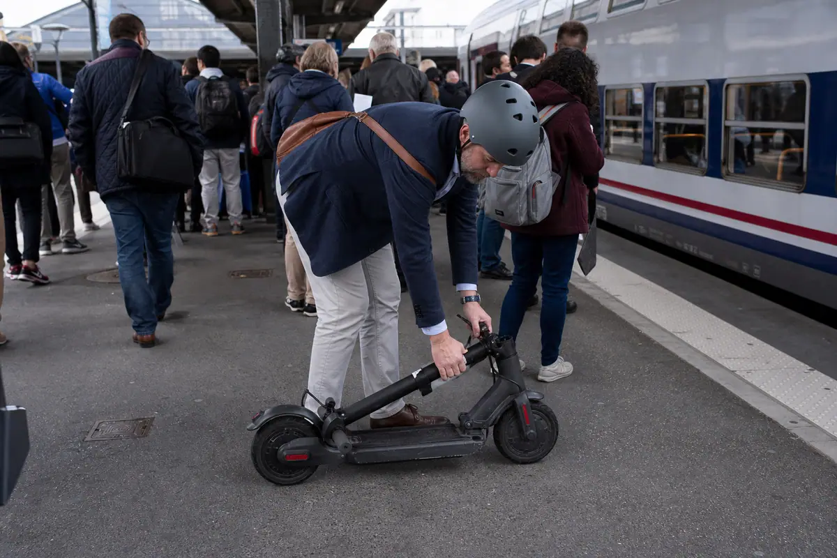 Un homme plie sa trottinette électrique sur le quai d'une gare avant de monter dans le train du matin