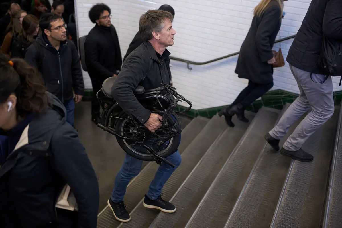 Un homme monte les escaliers du métro avec son vélo électrique pliant replié sous le bras