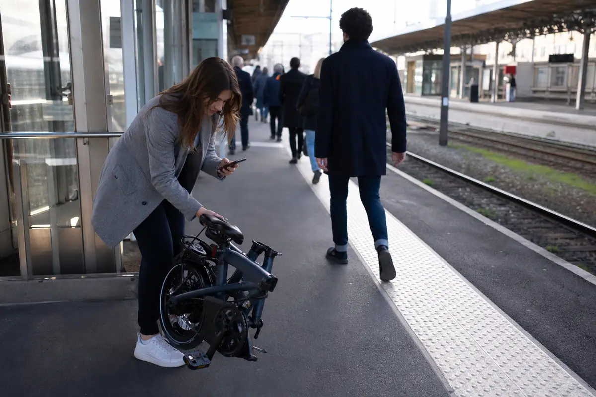 Une jeune femme déplie un vélo électrique pliant sur le quai d'une gare avant de partir travailler