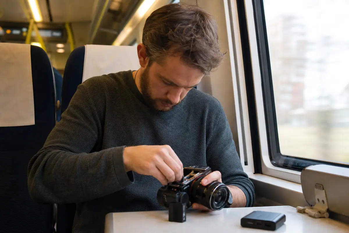 Un voyageur change la batterie de son appareil photo hybride dans un train