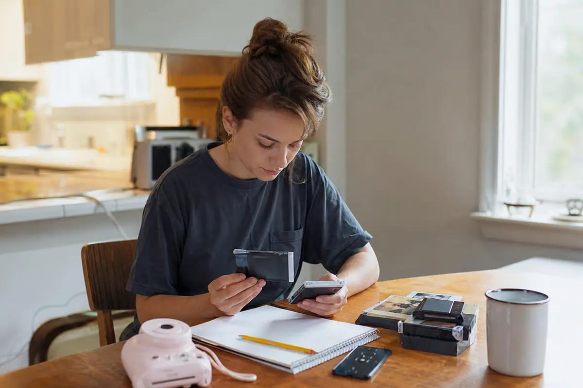 Une jeune femme calcule le budget film de son appareil photo instantané à l'aide d'une calculatrice