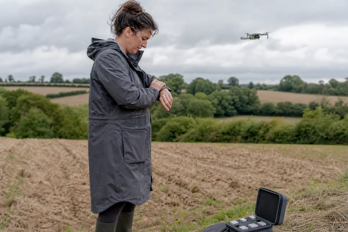 Une femme chronomètre le temps de vol de son drone dans un champ à la campagne