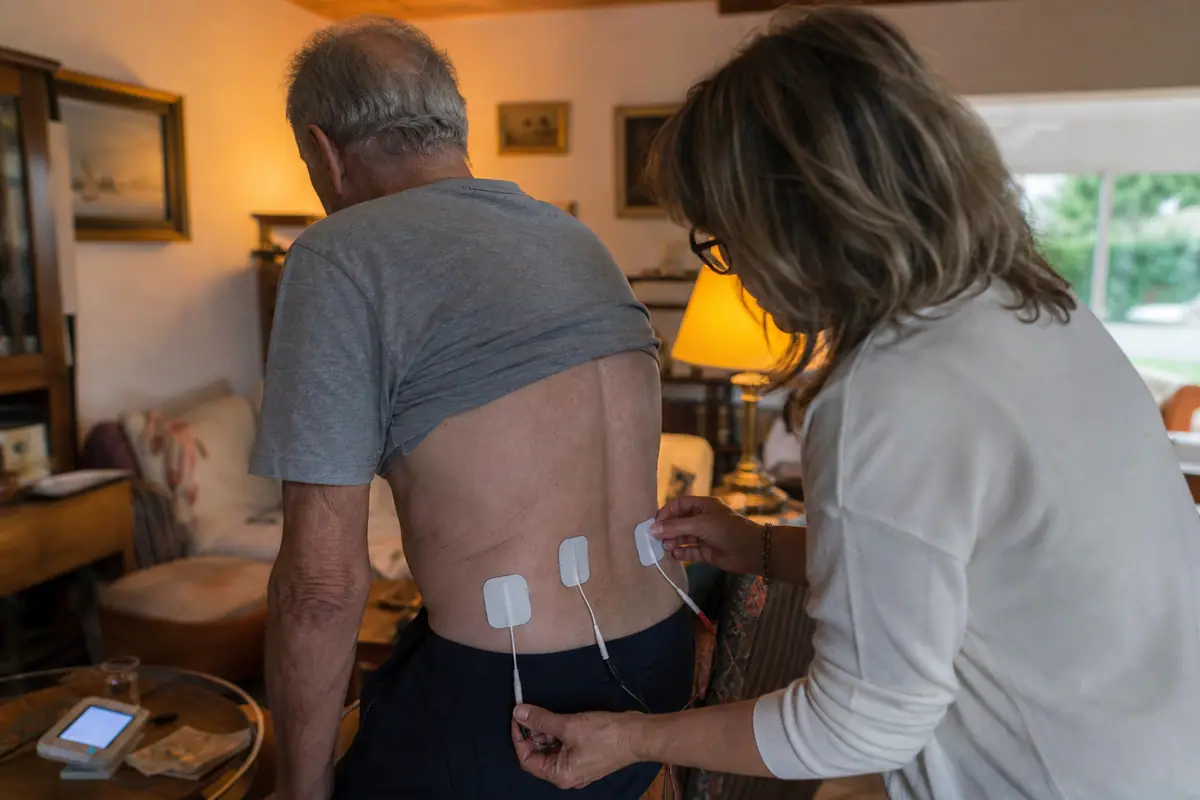 Une fille aide son père à placer des électrodes dans le bas du dos pour soulager une douleur musculaire