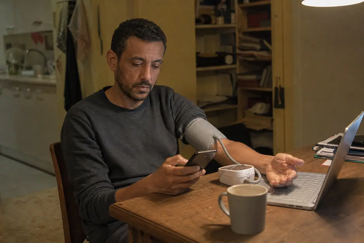 Un homme d'une quarantaine d'années prend sa tension le soir à son bureau et consulte le résultat sur son smartphone