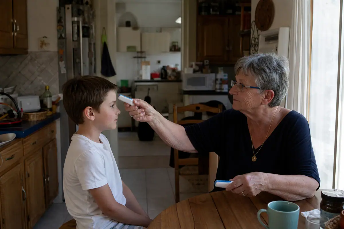 Une grand-mère compare deux méthodes de mesure de la température sur son petit-fils, l'une frontale et l'autre posée sur la table