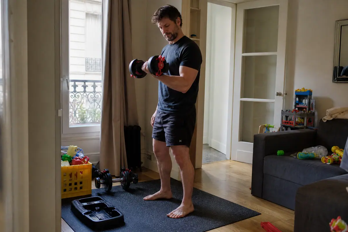 Un homme fait une série de curls biceps avec un haltère réglable dans un coin de son salon