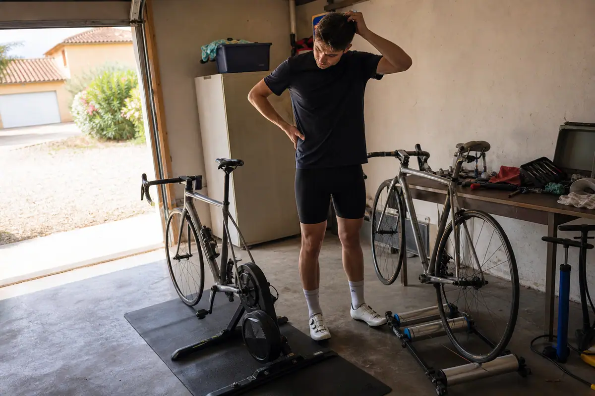 Un homme compare un home trainer à entraînement direct et un modèle sur roue installés côte à côte dans son garage