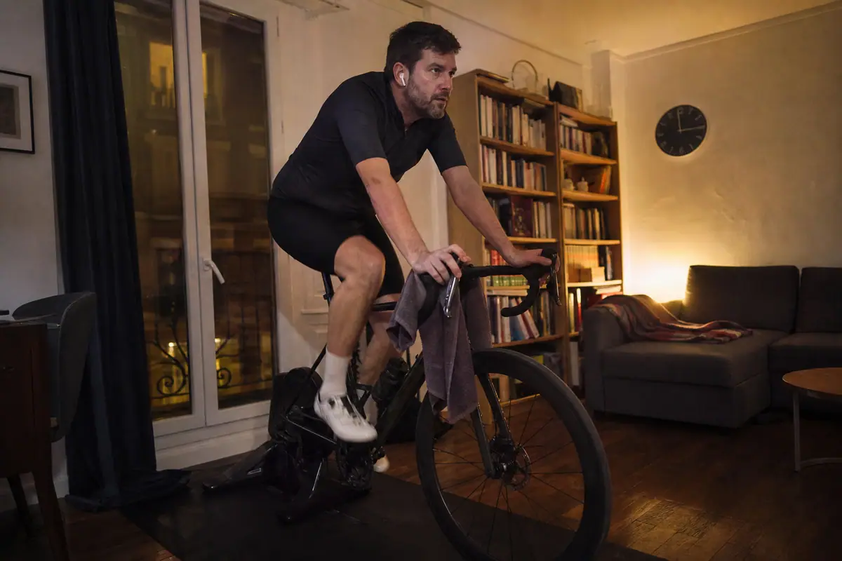 Un homme pédale tranquillement sur son home trainer en soirée dans le salon de son appartement, sur un tapis de protection épais