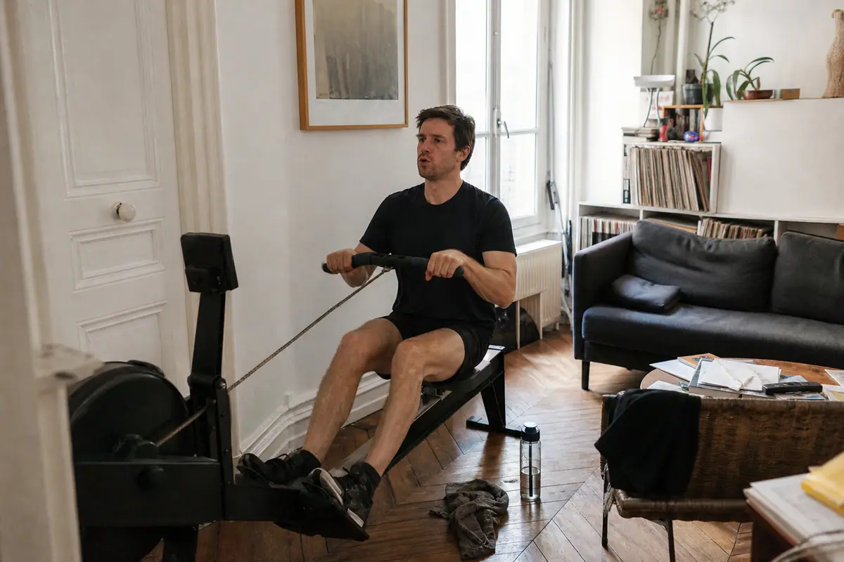 Un homme s'entraîne sur un rameur d'appartement installé dans un coin de son salon