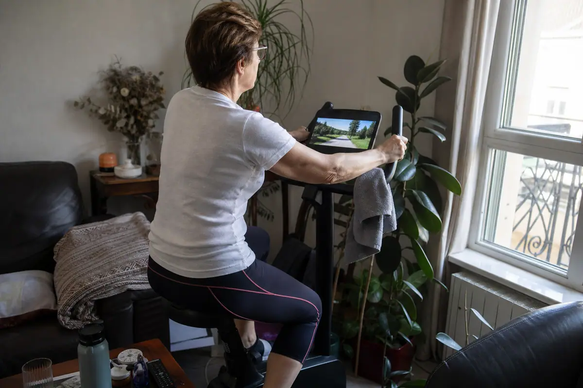 Une femme d'une cinquantaine d'années pédale sur un vélo d'appartement installé dans un coin de son salon