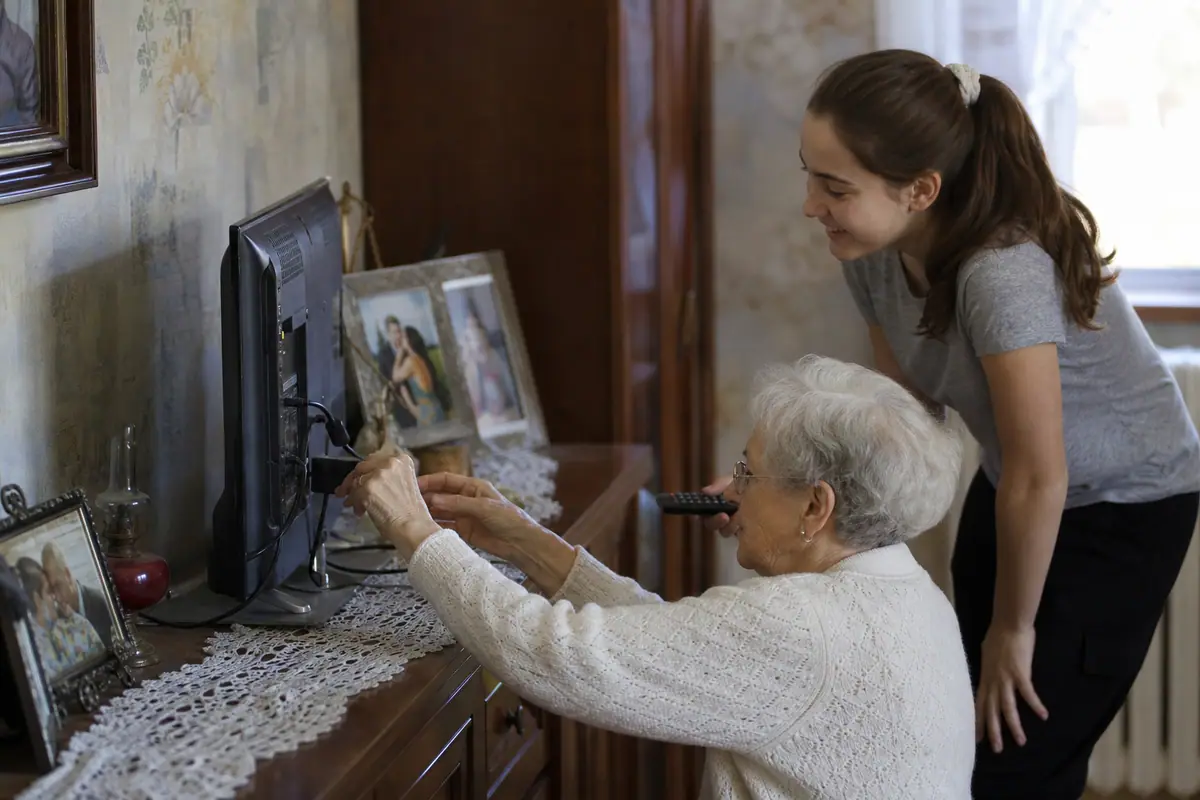 Une grand-mère branche une clé de streaming derrière son téléviseur avec l'aide de sa petite-fille
