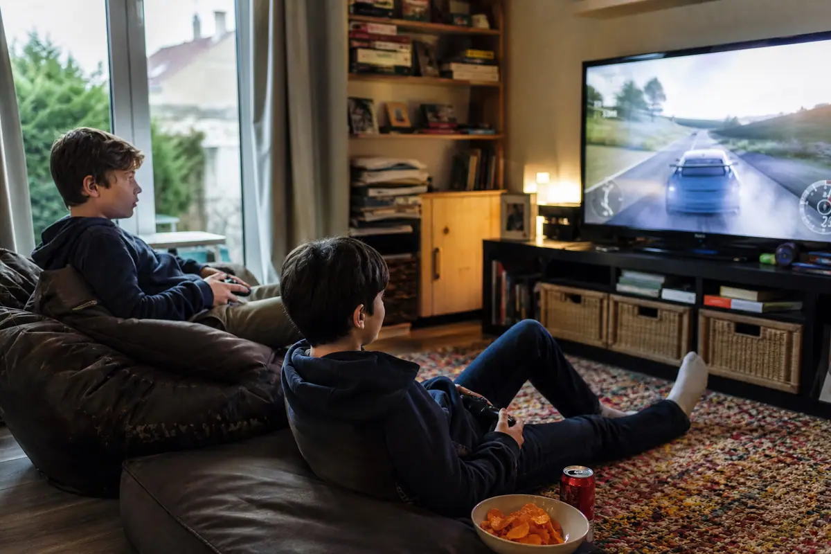 Deux adolescents jouent à un jeu de course sur un grand téléviseur dans le salon familial