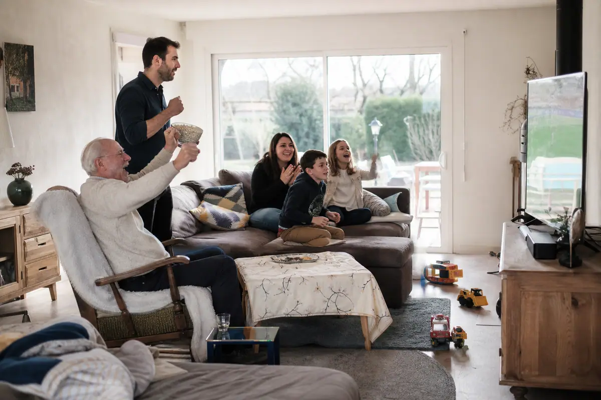 Une famille réunie sur trois générations regarde un match de football sur un grand téléviseur de 65 pouces