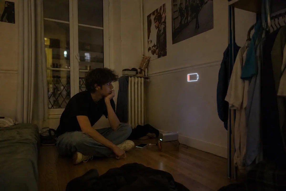 Un adolescent assis par terre dans sa chambre regarde un film projeté au mur en fin de soirée, près d'un vidéoprojecteur portable