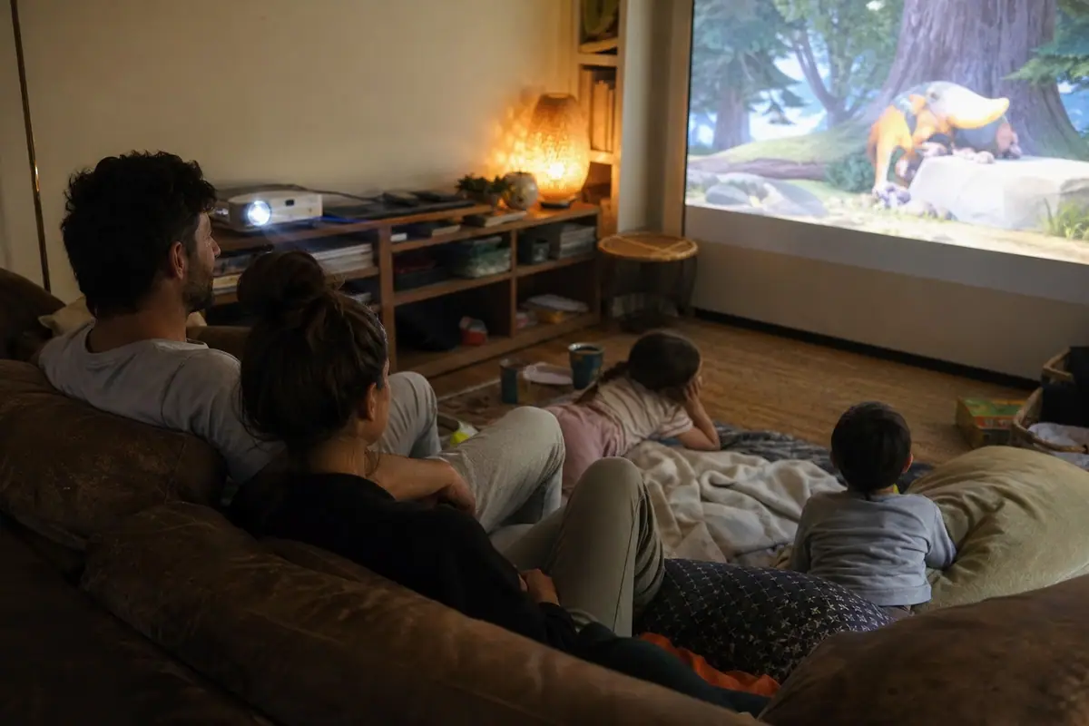 Une famille regarde un film projeté sur un grand écran blanc dans son salon, les enfants allongés sur des coussins
